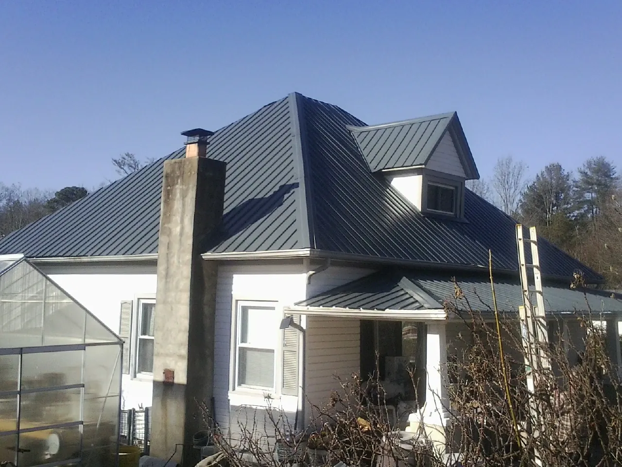 Dark blue standing seam metal roof on a white farmhouse with dormer — Slate & Tile Roof Repair by Roofing Brothers in Sunset Beach