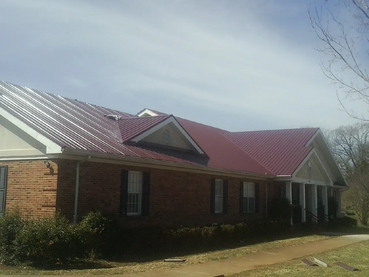 Red metal roof with gabled entries on a long brick building, from a Hail Damage Roof Repair job in Sunset Beach