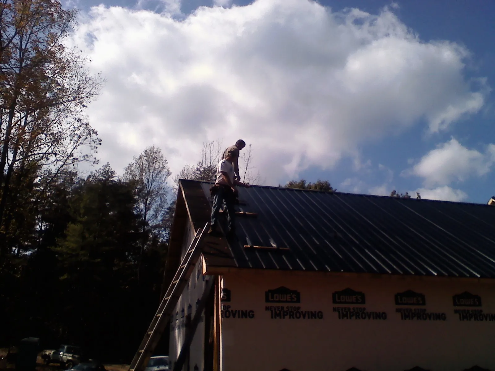 Roofer fastening dark metal panels high against a cloudy sky, from a Roof Inspection job in Sunset Beach