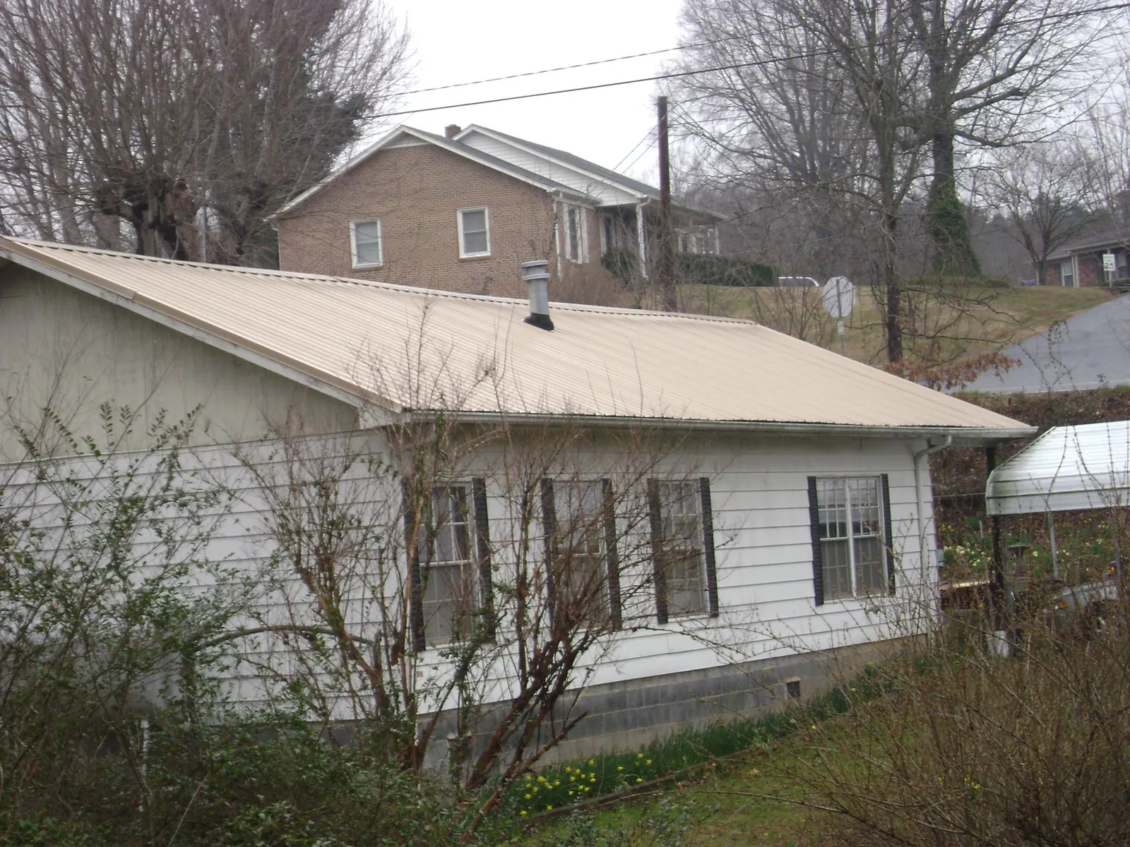 Tan metal roof on a white sided house set into a hillside — Commercial Roofing by Roofing Brothers in Sunset Beach