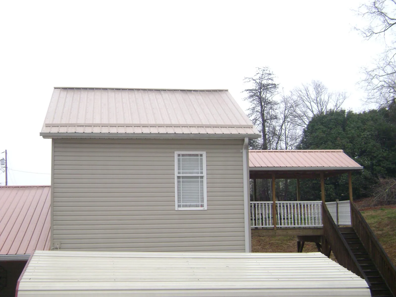 Tan metal roofs on a two story addition and attached porch, from a Roof Replacement job in Sunset Beach